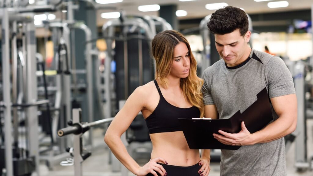 Two fitness enthusiasts review a workout plan on a clipboard in a gym.